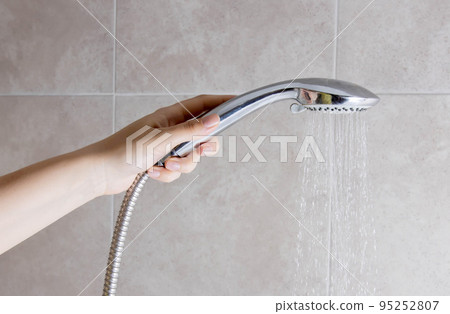 A woman holds a shower head in her hand against the background of a wall in the bathroom. Copy space for text 95252807
