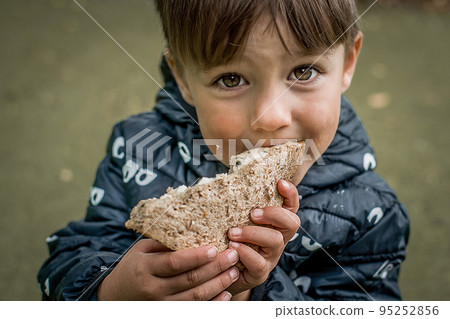 Portrait of hungry child boy looking with big eyes while eating bread. Poor refugee kid asking and looking for help. Crisis, peace, stop aggression, War in Ukraine. Sad refugee. 95252856