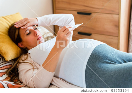 Pregnant thermometer temperature check. Pregnancy woman holding thermometer, check fever flu temperature. Pregnant girl sick. Concept of pregnancy, maternity, expectation for baby birth. Pregnant thermometer temperature check. Pregnancy woman holding thermometer, check fever flu temperature. Pregnant girl sick. Concept of pregnancy, maternity, expectation for baby birth. 95253194