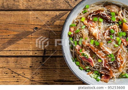 Spicy salad with pork pig ears, glass noodles, sesame seeds and green onions. Wooden background. Top view. Copy space Spicy salad with pork pig ears, glass noodles, sesame seeds and green onions. Wooden background. Top view. Copy space 95253600