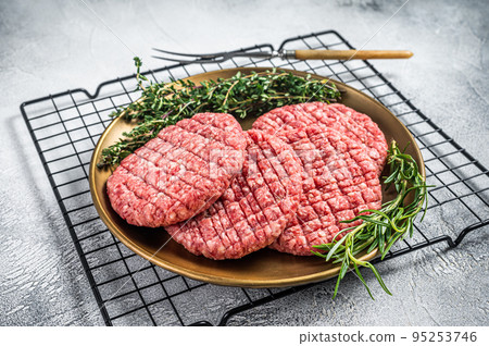 Raw minced beef burgers with spices on steel plate with rosemary and thyme. White background. Top view 95253746