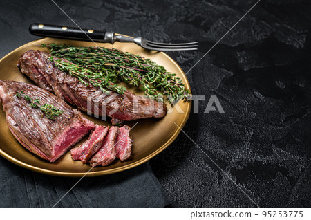 BBQ grilled Bavette Bavet beef meat steak with herbs on a plate. Black background. Top view. Copy space 95253775