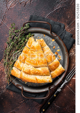 Slices of baked Round Borek cheese pie in kitchen tray with herbs. Dark background. Top view Slices of baked Round Borek cheese pie in kitchen tray with herbs. Dark background. Top view 95253830