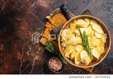 Homemade potato chips with sea salt and rosemary in wooden plate. Dark background. Top view. Copy space 95254055