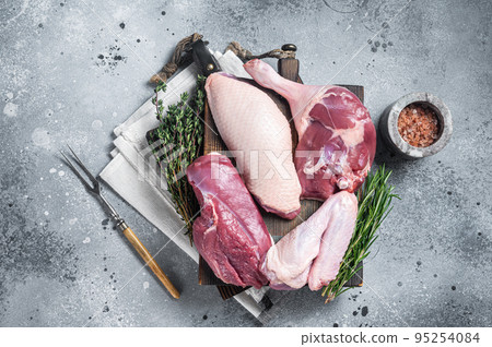 Butchered whole duck, raw breast steak, legs, wings on a butcher cutting board. Gray background. Top view 95254084