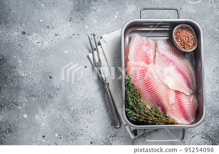 Raw white fish tilapia, uncooked fillet in kitchen tray with herbs. Gray background. Top view. Copy space Raw white fish tilapia, uncooked fillet in kitchen tray with herbs. Gray background. Top view. Copy space 95254098