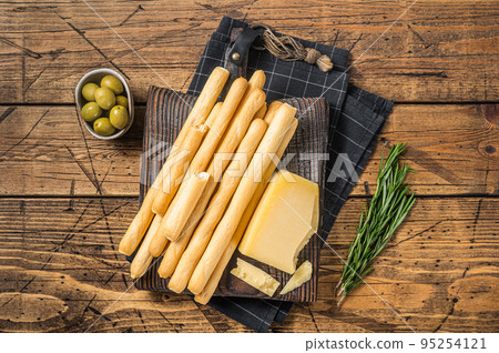 Traditional italian appetizer grissini bread sticks on wooden board with olives and parmesan cheese. Wooden bakground. Top view 95254121