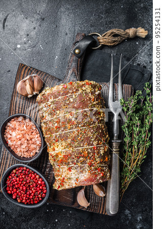 Uncooked spicy pork meat roulade prepared to roast with herbs and spices. Black background. Top view Uncooked spicy pork meat roulade prepared to roast with herbs and spices. Black background. Top view 95254131
