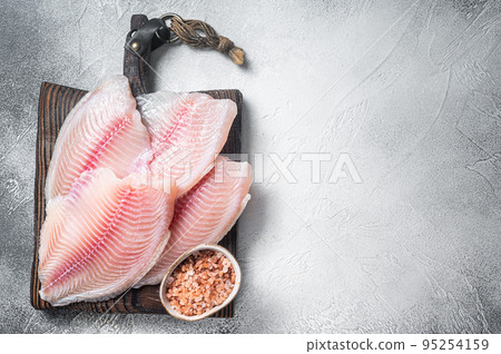 Uncooked tilapia fish fillet on a wooden board. White background. Top view. Copy space Uncooked tilapia fish fillet on a wooden board. White background. Top view. Copy space 95254159