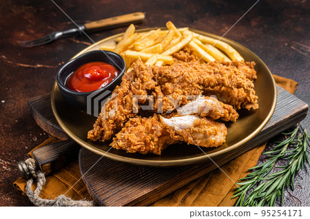 Fried Breaded chicken tender strips with french fries and tomato ketchup on a plate. Dark backgrund. Top view Fried Breaded chicken tender strips with french fries and tomato ketchup on a plate. Dark backgrund. Top view 95254171