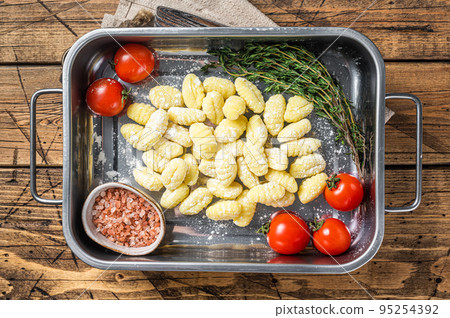Uncooked Raw potato gnocchi in kitchen steel tray with herbs. Wooden background. Top view Uncooked Raw potato gnocchi in kitchen steel tray with herbs. Wooden background. Top view 95254392