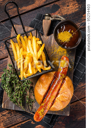Currywurst Bratwurst sausage in a bun with curry sauce and French fries. Wooden background. Top view Currywurst Bratwurst sausage in a bun with curry sauce and French fries. Wooden background. Top view 95254403