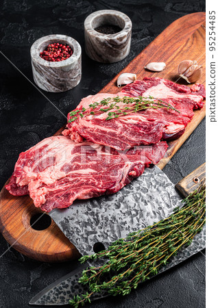 Butcher marbled meat Steaks on wooden cutting board, raw beef rib-eye steaks. Black background. Top view 95254485
