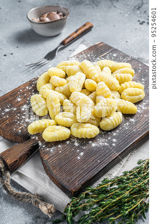 Raw homemade potato gnocchi with fork on wooden cutting board. Gray background. Top view Raw homemade potato gnocchi with fork on wooden cutting board. Gray background. Top view 95254601