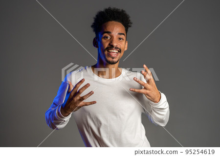 Young energetic african american man in white wear smiling and dancing in good mood on brown Young energetic african american man in white wear smiling and dancing in good mood on brown 95254619