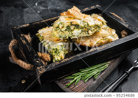 Spinach pie pieces, Spanakopita Greek Pie in wooden tray. Black background. Top view Spinach pie pieces, Spanakopita Greek Pie in wooden tray. Black background. Top view 95254686