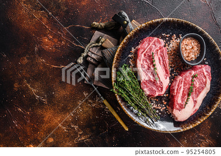 Chuck eye Roll beef steaks, raw meat on a plate with thyme and herbs. Dark background. Top view. Copy space 95254805