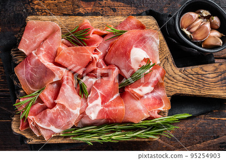 Slices of jamon serrano ham or prosciutto crudo parma on wooden board with rosemary. Wooden background. Top view Slices of jamon serrano ham or prosciutto crudo parma on wooden board with rosemary. Wooden background. Top view 95254903