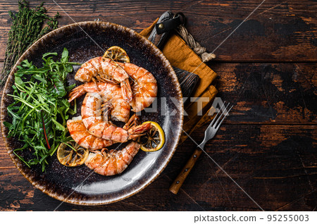 Spicy garlic Giant shrimps prawns in plate with salad. Wooden background. Top view. Free copy space Spicy garlic Giant shrimps prawns in plate with salad. Wooden background. Top view. Free copy space 95255003