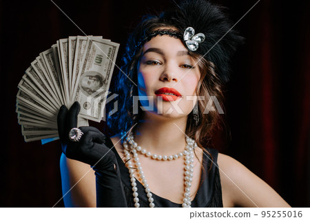 Rich luxurious woman dressed in Art Deco style waves a bundle of dollars banknotes like fan. Vintage Rich luxurious woman dressed in Art Deco style waves a bundle of dollars banknotes like fan. Vintage 95255016