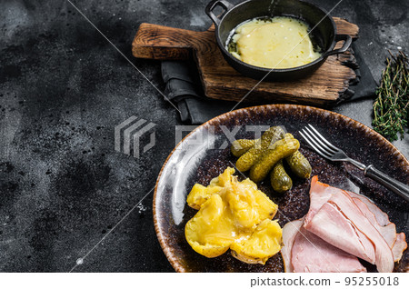 Raclette Melted cheese with boiled potato and ham on rustic plate, swiss meal. Black background. Top view. Copy space 95255018