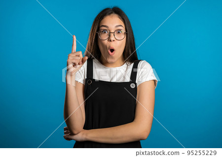 Portrait of young asian thinking pondering girl having idea moment pointing finger up on blue studio 95255229
