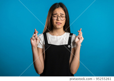 Cute asian young girl praying over blue background. Woman in glasses begging someone. Cute asian young girl praying over blue background. Woman in glasses begging someone. 95255261