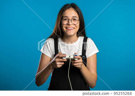 Pretty asian girl playing video exciting game on Tv with joystick on blue studio wall. Using modern Pretty asian girl playing video exciting game on Tv with joystick on blue studio wall. Using modern 95255268