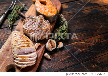 Barbecue grilled steaks - salmon, beef rib eye and turkey breast fillet on a wooden board. Wooden background. Top view. Copy space 95255634
