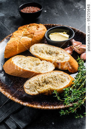 Garlic Spread on Toasted Baguette with Salt, Pepper, Thyme and Olive Oil in plate. Black background. Top view Garlic Spread on Toasted Baguette with Salt, Pepper, Thyme and Olive Oil in plate. Black background. Top view 95255648