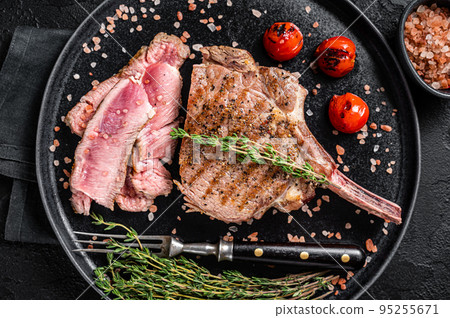 Barbecue sliced rib eye Tomahawk beef (veal) steak on a plate with pink salt. Black background. Top view 95255671