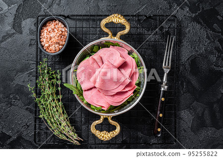 Thin slices of ham in a skillet with arugula salad. Black background. Top view Thin slices of ham in a skillet with arugula salad. Black background. Top view 95255822