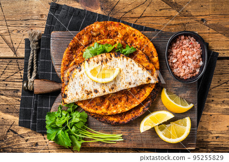 Turkish cuisine made with thin dough and minced beef meat lahmacun on wooden board with herbs. Wooden background. Top view Turkish cuisine made with thin dough and minced beef meat lahmacun on wooden board with herbs. Wooden background. Top view 95255829