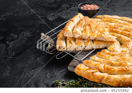 Turkish Tepsi Boregi, Round Borek cheese pie on kitchen board. Black background. Top view. Copy space 95255842