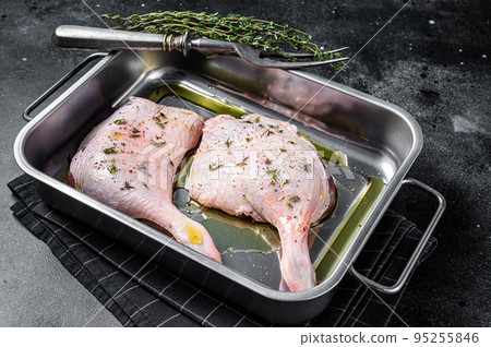 Raw meat, duck legs thighs with herbs and ingredients in a steel tray. Black background. Top view 95255846