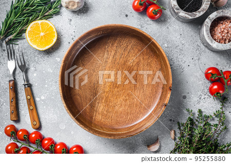 Food cooking and healthy eating background with empty rustic plate and fresh seasoning, knife, fork and vegetables ingredients. Gray background. Top view. Copy space 95255880