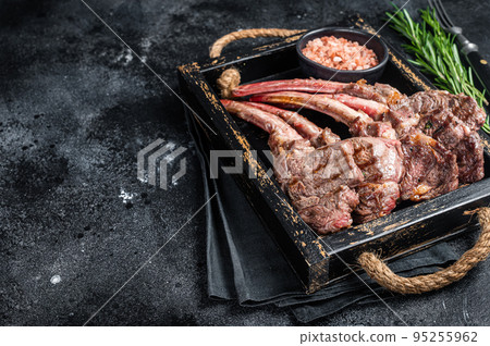 Grilled lamb chop steak, mutton meat cutlet in wooden tray. Black background. Top view. Copy space Grilled lamb chop steak, mutton meat cutlet in wooden tray. Black background. Top view. Copy space 95255962
