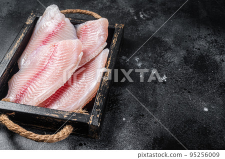 Fresh tilapia white fish fillet in a wooden tray. Black background. Top view. Copy space Fresh tilapia white fish fillet in a wooden tray. Black background. Top view. Copy space 95256009
