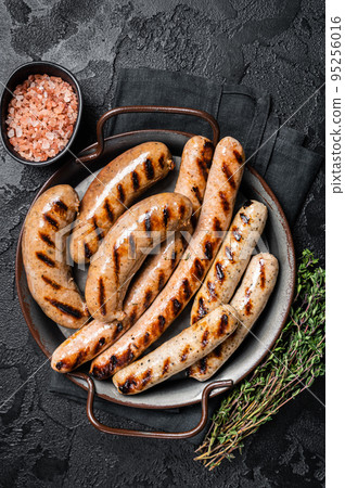 Grilled Bratwurst meat sausages on a steel tray with herbs. Black background. Top view 95256016