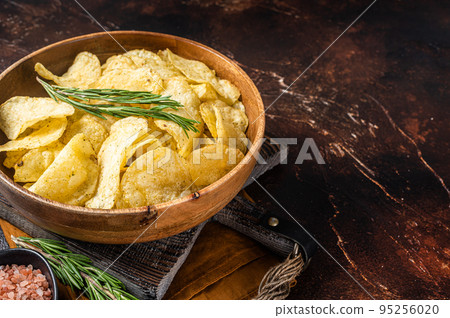 Homemade potato chips with sea salt and rosemary in wooden plate. Dark background. Top view. Copy space Homemade potato chips with sea salt and rosemary in wooden plate. Dark background. Top view. Copy space 95256020