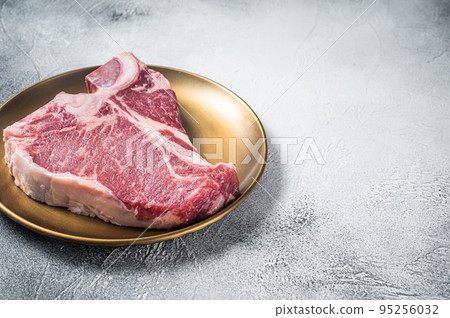 Raw T-bone porterhouse beef meat Steak on golden metalic plate. Gray background. Top view. Copy space 95256032