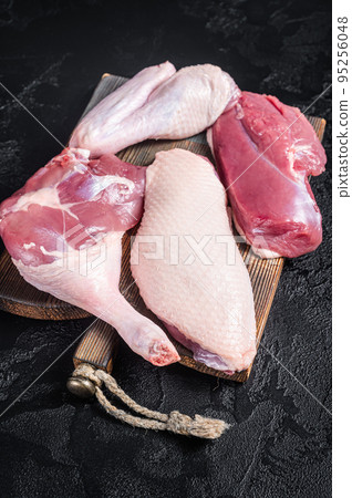 Duck breast fillet, legs, wings, raw meat on a butcher cutting board. Black background. Top view Duck breast fillet, legs, wings, raw meat on a butcher cutting board. Black background. Top view 95256048