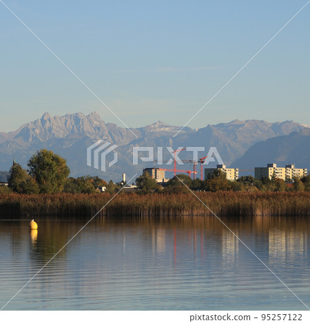 Houses in Wetzikon, shore of Lake Pfaeffikersee and mountain ranges. Houses in Wetzikon, shore of Lake Pfaeffikersee and mountain ranges. 95257122