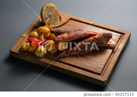fried surmullet fish with potato and lemon on wooden board on black background 95257133