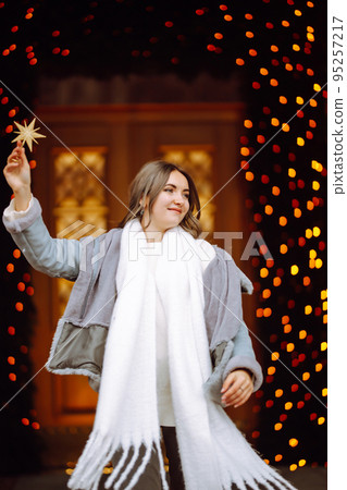 Smiling woman in winter style clothes posing at festive street market. Young woman enjoying winter moments. 95257217