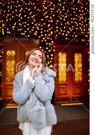 Smiling woman in winter style clothes posing at festive street market. Young woman enjoying winter moments. 95257218