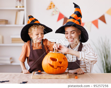 Son and mom making Jack-o-Lantern together at home, carving Halloween pumpkin 95257256