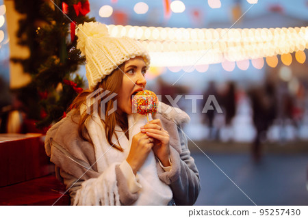 Young woman with caramel apple on Christmas market. Smiling woman in winter style clothes posing. 95257430