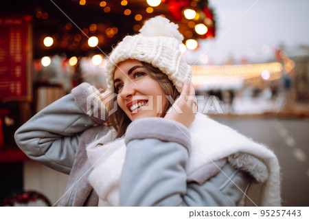 Smiling woman in winter style clothes posing at festive street market. Young woman enjoying winter moments. Smiling woman in winter style clothes posing at festive street market. Young woman enjoying winter moments. 95257443