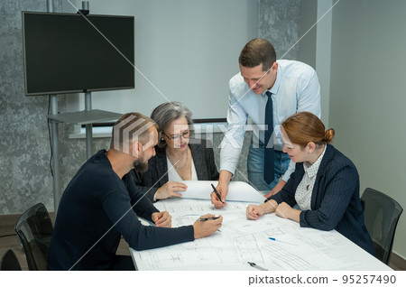 The boss gives instructions to three employees in the office conference room. Brainstorming engineers and architects. The boss gives instructions to three employees in the office conference room. Brainstorming engineers and architects. 95257490